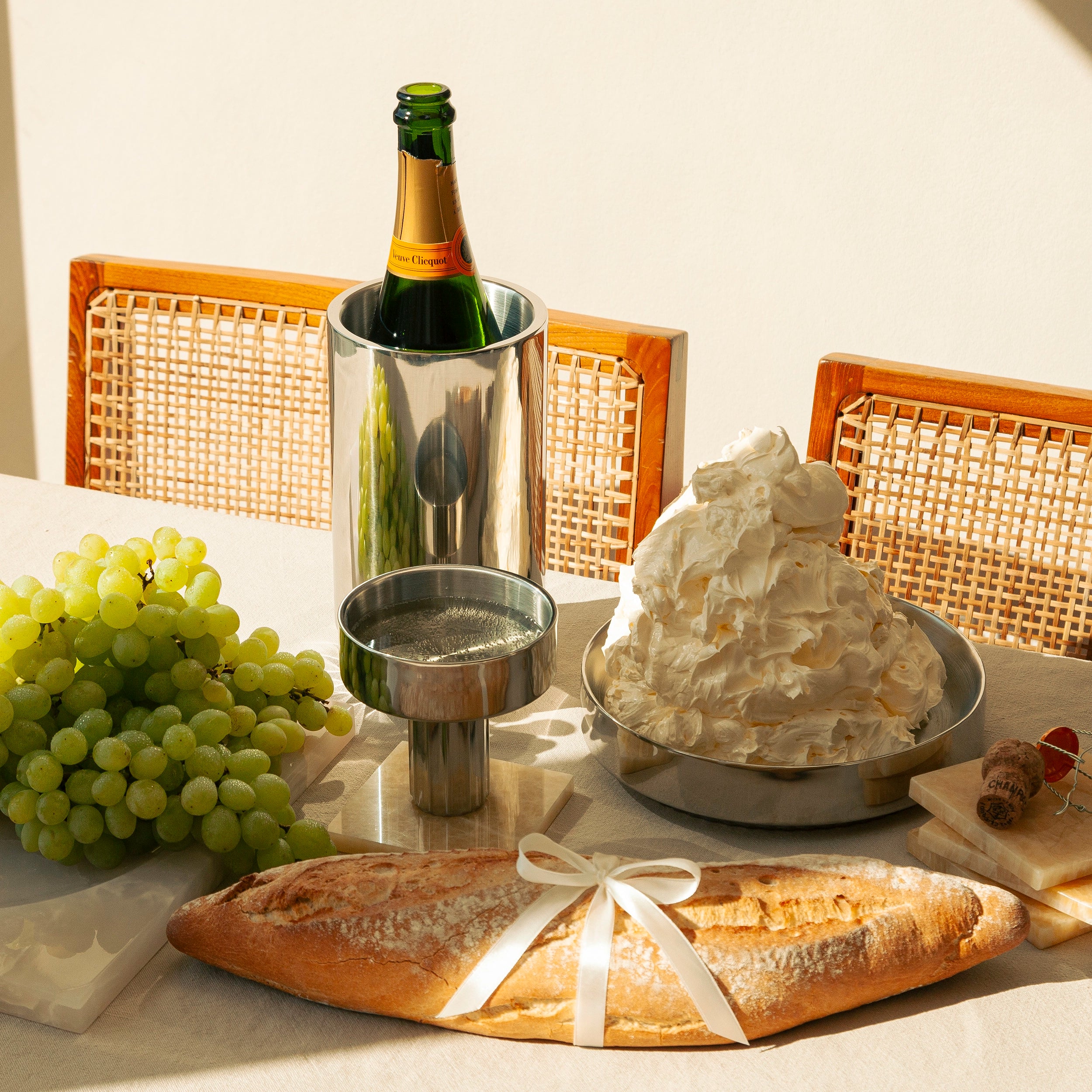 Tablesetting Styling with Wine Cooler and Champagne Bottle and Steel Coupé filled with Champagner on a Honey Onyx Coaster next to a Steel Plate with butter cream and fresh bread